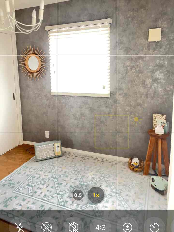 ダークグレーの壁とホワイトブラインドがあるコンパクトなワンルーム、ヴィンテージ風ラグと木目調のスツールが配置された自然な雰囲気のインテリア