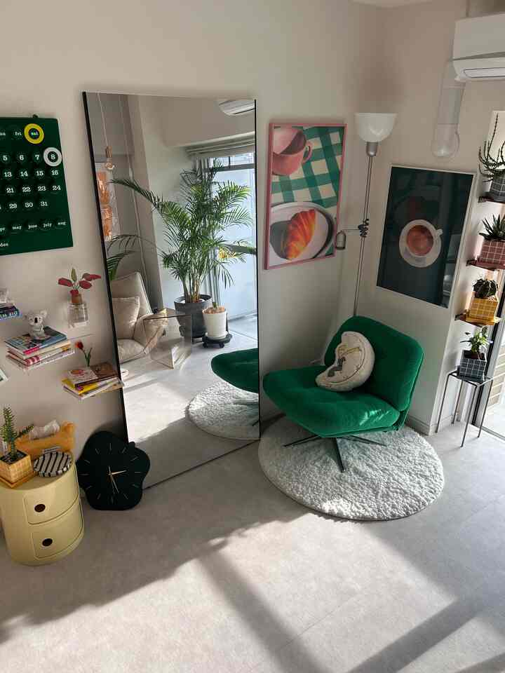 白い壁と床に、緑のアームチェアと大きな全身鏡、観葉植物が配置された明るい自然光あふれるリビング
