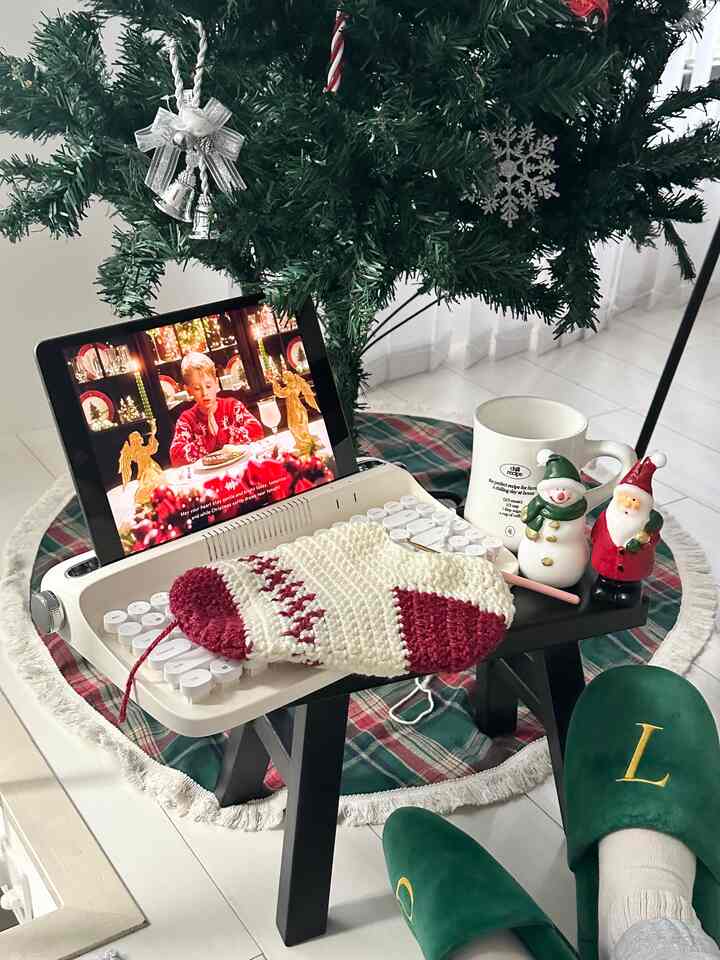 白を基調に赤のアクセントが映えるリビングのクリスマス装飾、キーボードに編み物の靴下と小物が置かれた雰囲気のあるインテリア