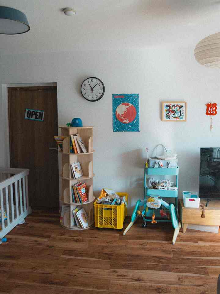 白い壁と木目調の床の子供部屋、絵本棚とベビーベッド、収納カートが配置された印象的な空間