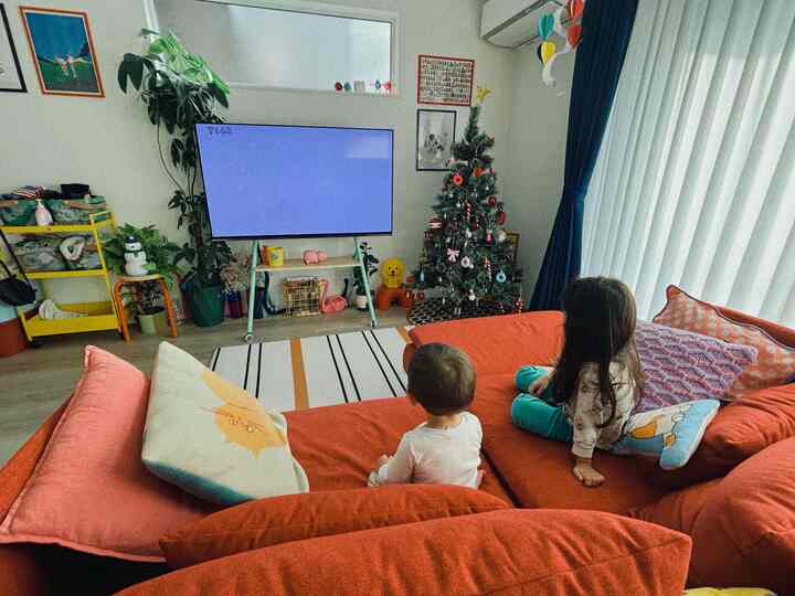 オレンジ色のソファを中心としたリビング、テレビとクリスマスツリー、子供たちが座る居心地の良い空間