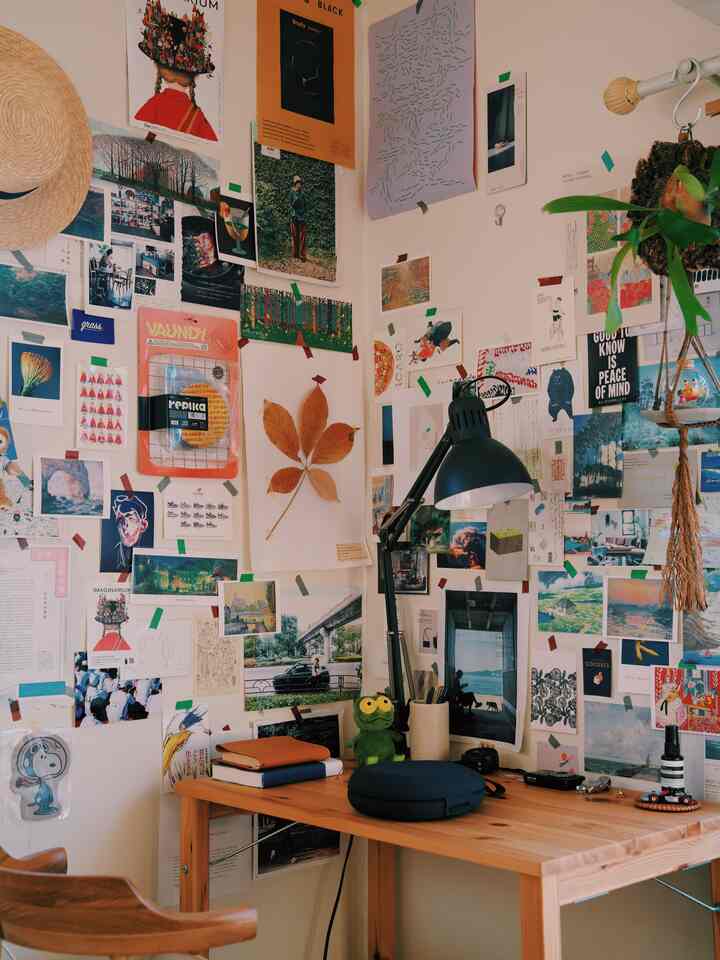 ナチュラルウッドトーンと白い壁が調和した一人暮らし用コンパクトなデスク空間、多彩なポスターが壁に貼られた雰囲気のある読書向けホームオフィス