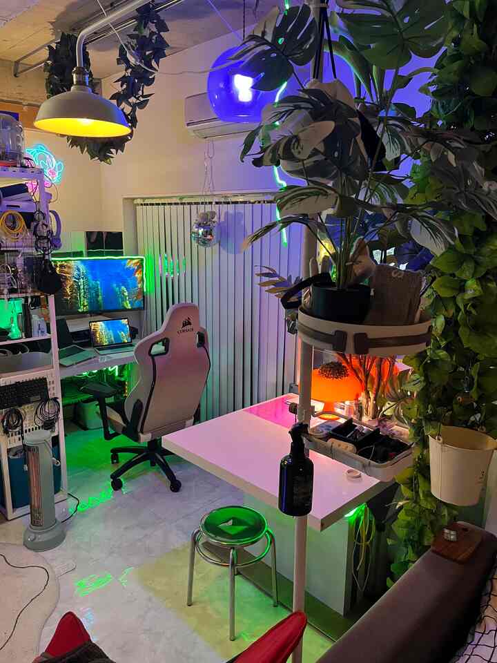 白と緑のトーンのワンルーム、ゲーミングチェアと多くの植物が配置された居心地の良いホームオフィス空間