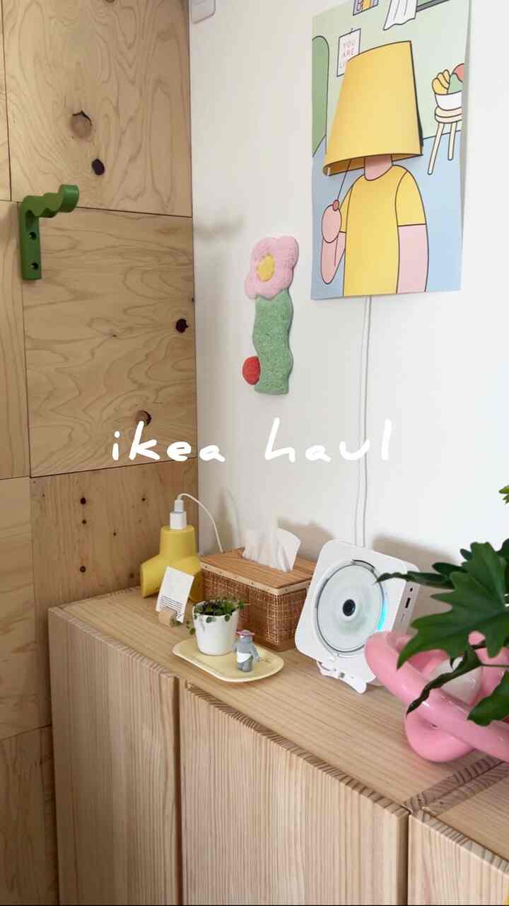 ナチュラルカラーのリビング空間、木製キャビネットの上に黄色のテーブルランプとピンクの花瓶、緑の植物が配置された雰囲気のあるインテリア