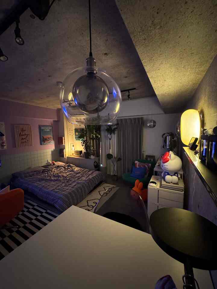 Modern compact bedroom with a central transparent pendant light, colorful cushions, and posters decorating the space