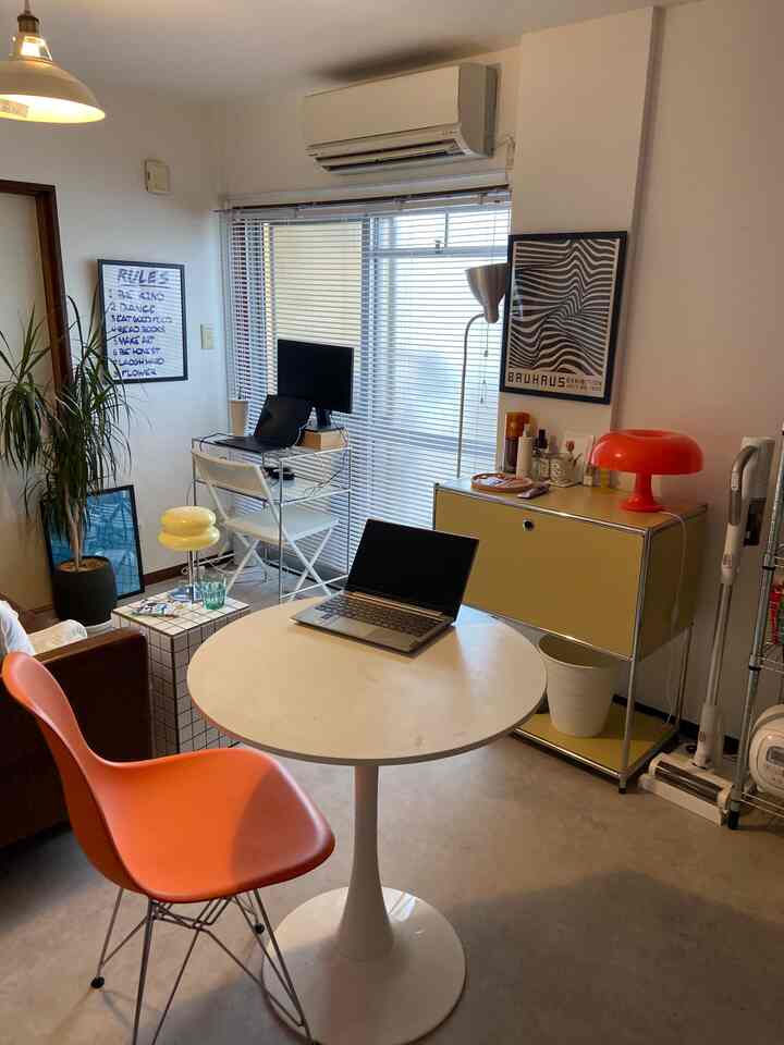 白を基調とした1DKの一人暮らし用リビング、オレンジの椅子とホームオフィス設備が配置された雰囲気のあるインテリア