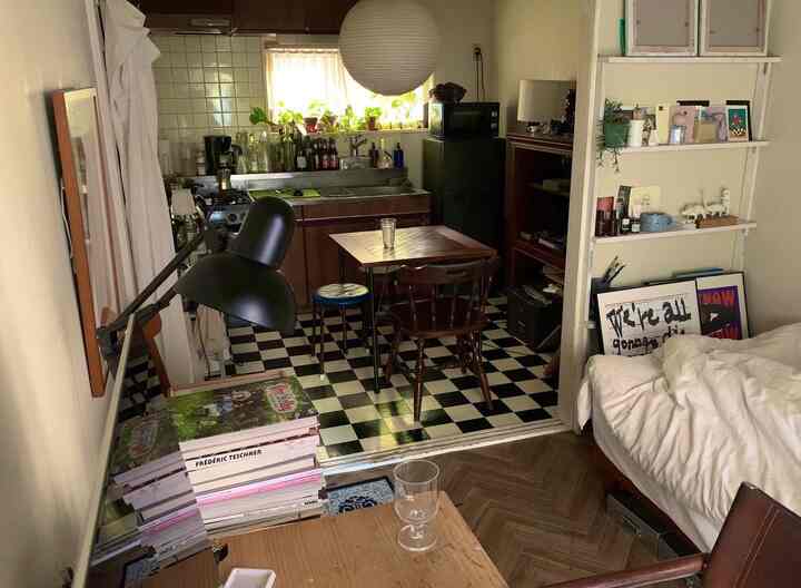 白と黒を基調としたワンルームのキッチンと寝室空間、コンパクトなダイニングテーブルとデスクが配置された雰囲気のあるインテリア