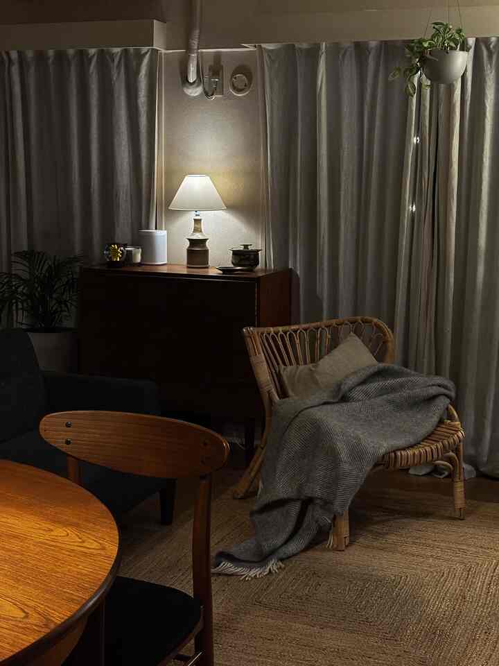 暖色系の照明が灯るリビング空間、ラタンチェアとヴィンテージのテーブルランプが印象的なインテリア