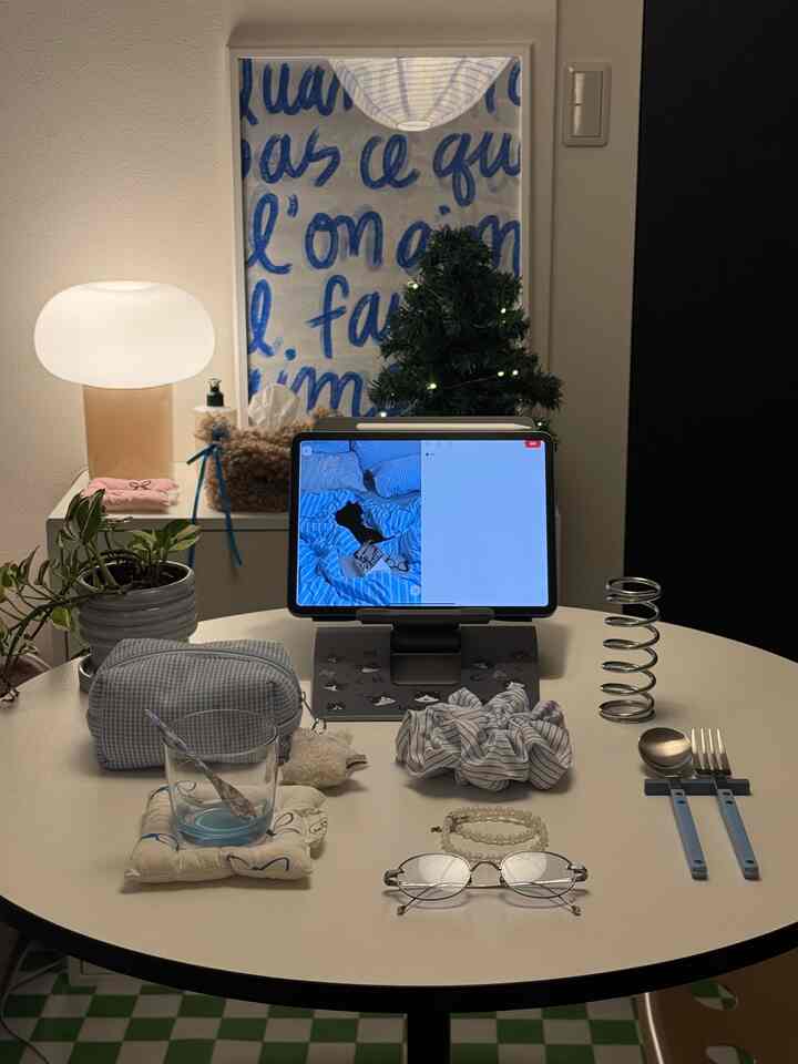 ブルーとホワイトの色調が特徴のワンルーム、丸テーブルとタブレット、テーブルランプが配置されたモダンでミニマルなワークスペース