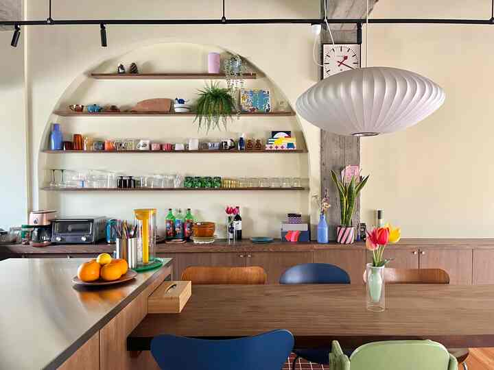 白と木目調の調和が取れたキッチンとダイニングルーム、ミッドセンチュリーモダンのダイニングテーブルとペンダントライトが配置されたカフェ風の雰囲気のあるインテリア