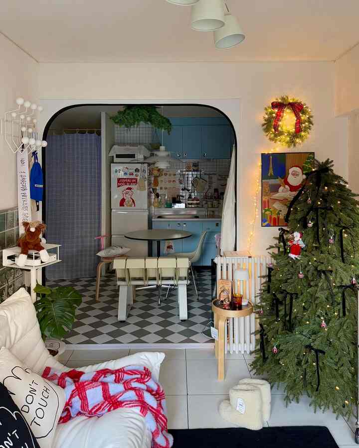 白とナチュラルトーンのリビングとキッチン、クリスマスツリーと赤いチェック柄のスローが配置された暖かい雰囲気のインテリア