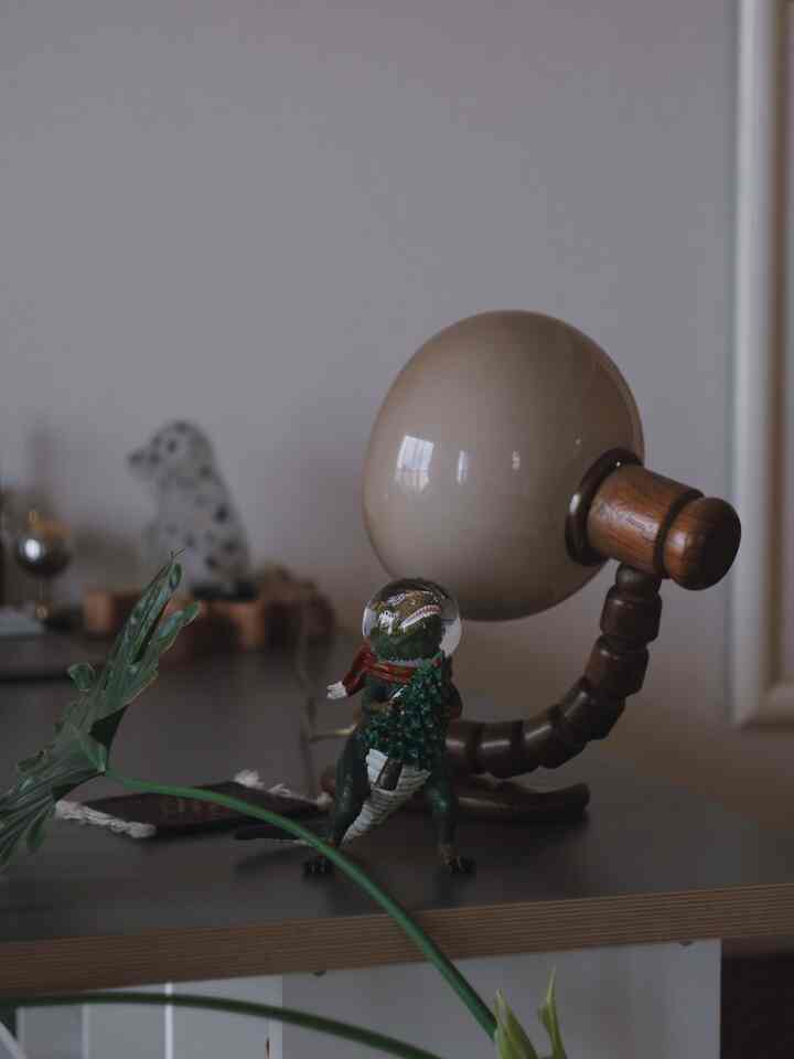 Natural-toned workspace desk featuring a dinosaur snow globe with a Christmas scarf and wooden lamp, creating a cozy atmosphere