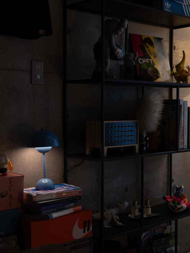 暗いコンクリート壁を背景に、青いテーブルランプと黒い金属の棚が並ぶ一人暮らしのモダンな空間