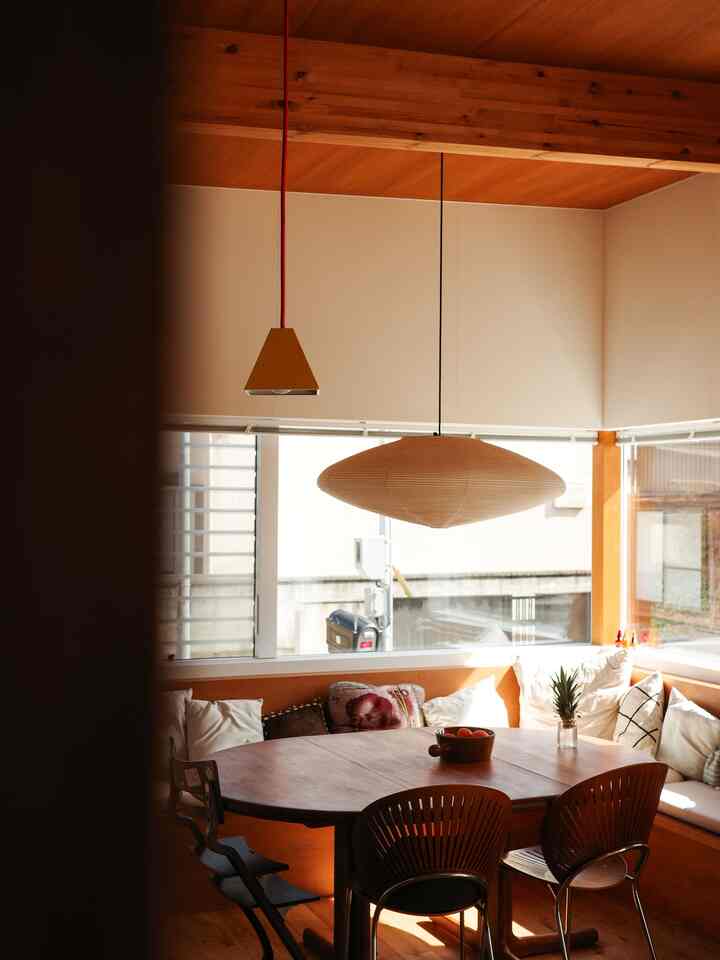 ナチュラルな木目調のコーナー窓があるダイニング、ペンダントライトとベンチ席が配置された暖かみのある空間