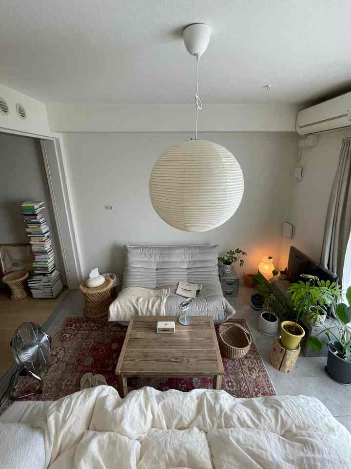 White and red toned 1LDK living room featuring natural sofa, wooden coffee table, and numerous plants creating a cozy atmosphere