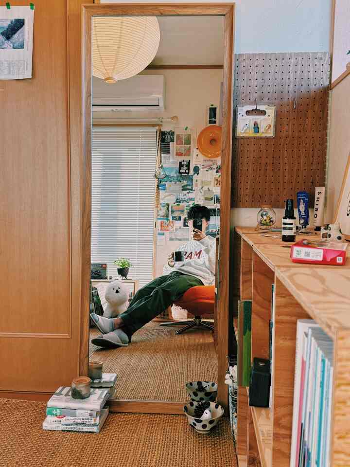 ナチュラルカラーのリビングルーム、大きな全身鏡とオレンジ色のアームチェア、ラグ、本棚が配置された雰囲気のあるインテリア