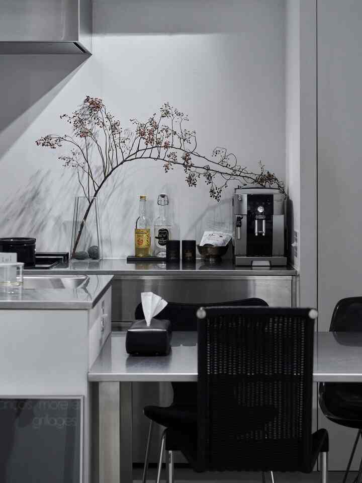 モノトーンとステンレス家具が調和したキッチン、コーヒーマシンと花瓶が配置されたシンプルで清潔感のあるインテリア