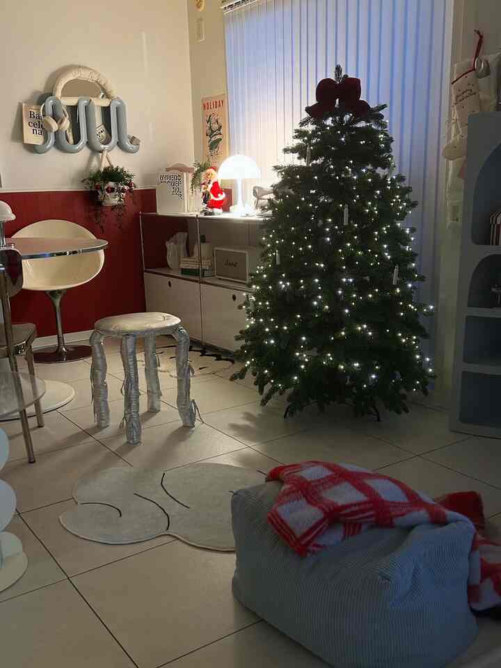 白と赤のトーンが調和したリビング、電飾が施されたクリスマスツリーとテーブルランプが温かみのある雰囲気を醸し出すインテリア