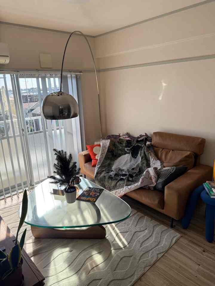 Beige and natural toned living room featuring a leather sofa, glass coffee table, and arc floor lamp in a cozy atmosphere