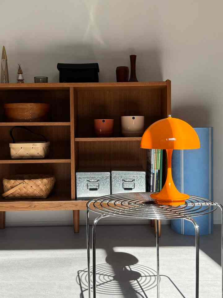 Natural modern space with wooden shelf unit and metal stool topped with vibrant orange lamp