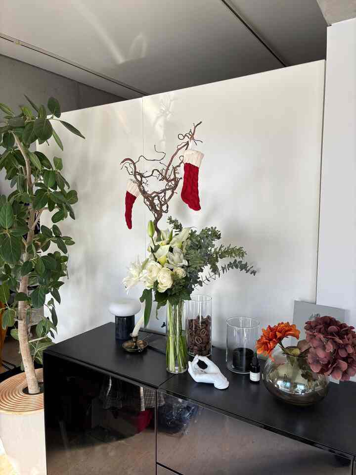 白い壁と黒いキャビネットのワンルーム空間、花瓶や植物、クリスマスの靴下が配置された雰囲気のあるインテリア
