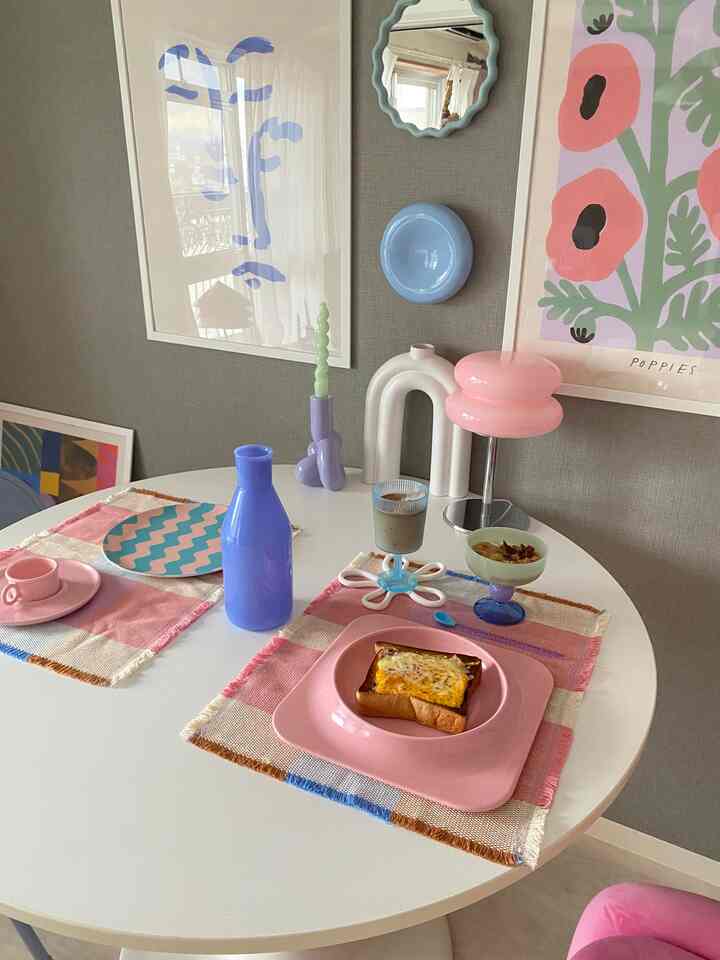 ピンクとホワイトのトーンが特徴の4人用丸テーブルのダイニング、スタイリッシュなテーブルウェアとアートポスターが配置されたモダンな空間