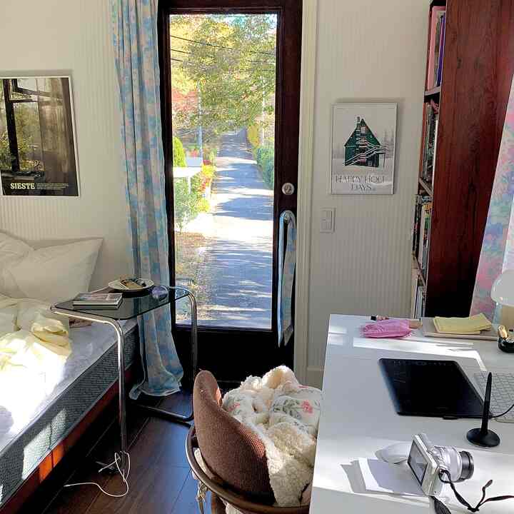 白と木目調を基調としたワンルーム寝室、青い花柄カーテンと机が配置された雰囲気のあるホームオフィス空間