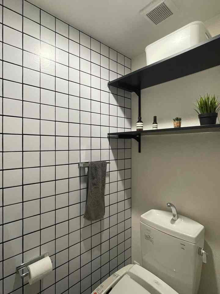 A white and black toned restroom featuring tiled wall, black shelves, towel, and small plants creating a clean atmosphere