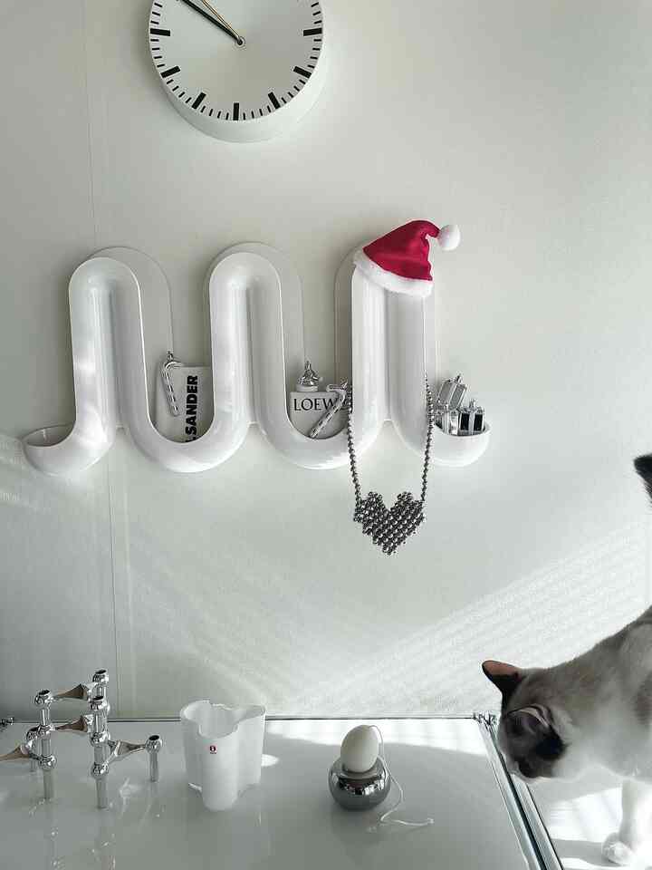 明るい白いトーンの壁に曲線を描く壁掛けシェルフと時計、猫がいるミニマルなインテリア