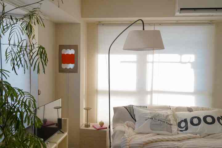 白とベージュのトーンのリビング、ソファとフロアランプ、ポスターが配置された雰囲気のある空間