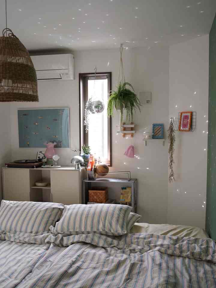 白と緑の色調の寝室、ストライプの寝具と植物が配置され、落ち着いた自然な雰囲気のインテリア