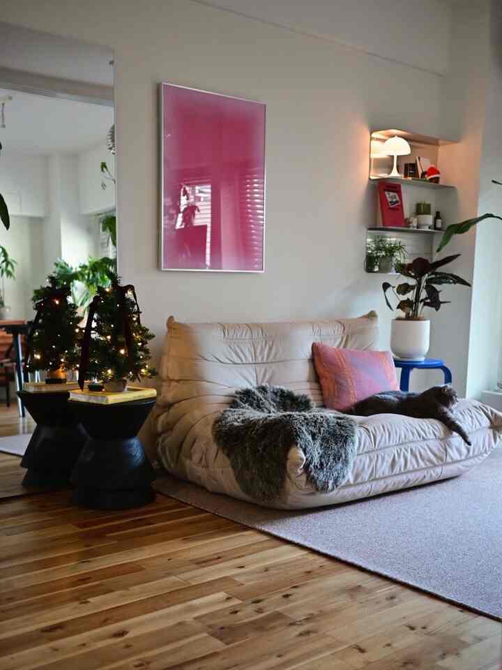 Living room with white walls and light brown wooden floor, featuring a cream sofa, mini Christmas trees, and a cat comfortably resting