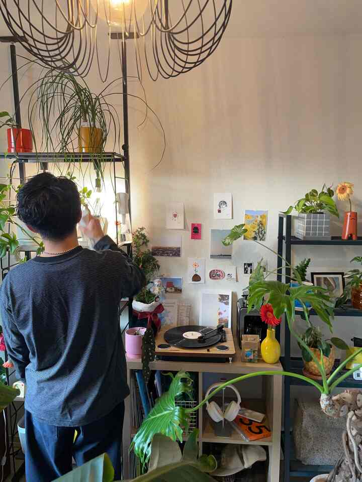 ナチュラルトーンのコンパクトなリビングルーム、さまざまな観葉植物とレコードプレーヤー、棚が調和したミッドセンチュリーモダンスタイルの空間