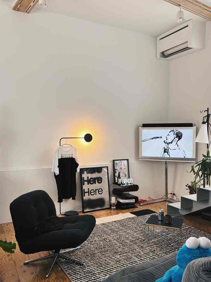 モノトーンのリビングルーム、中央にアームチェアとラグが配置され、ポスターとテレビが調和したシンプルで印象的なミッドセンチュリーモダンインテリア