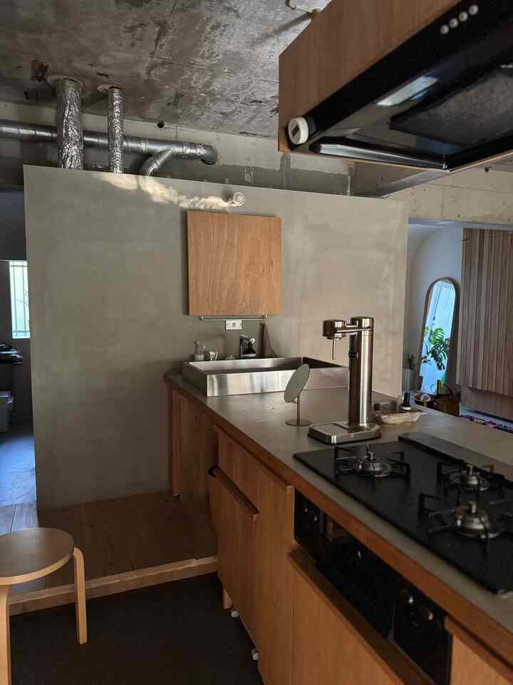Natural wood tone studio kitchen with exposed concrete ceiling, featuring a custom kitchen counter and integrated washbasin in a natural modern style