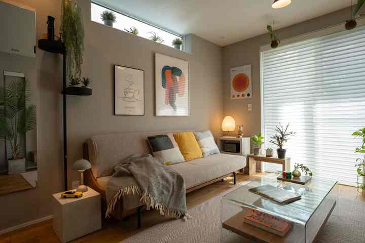 グレーとナチュラルな色調のリビング、ソファベッドとガラスのコーヒーテーブル、植物が配置された雰囲気のある空間