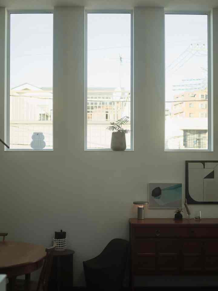 白い壁とブラウンの木製家具が置かれた北欧風ダイニング、自然光が差し込む大きな窓が特徴の印象的な空間