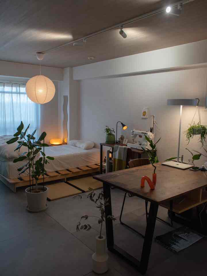 ナチュラルな木目調と和モダンスタイルのワンルーム、ベッドとデスク、多様な照明と植物が配置された印象的な空間