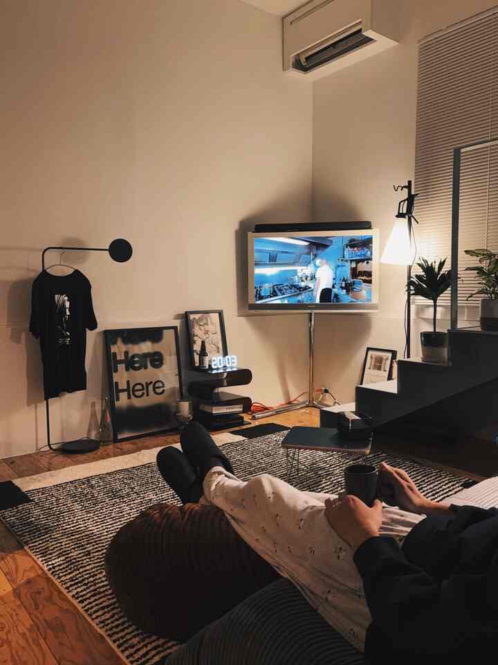 暖かな照明がともるモノトーンのリビング、テレビやラグが配置され、ミッドセンチュリーの雰囲気ある空間