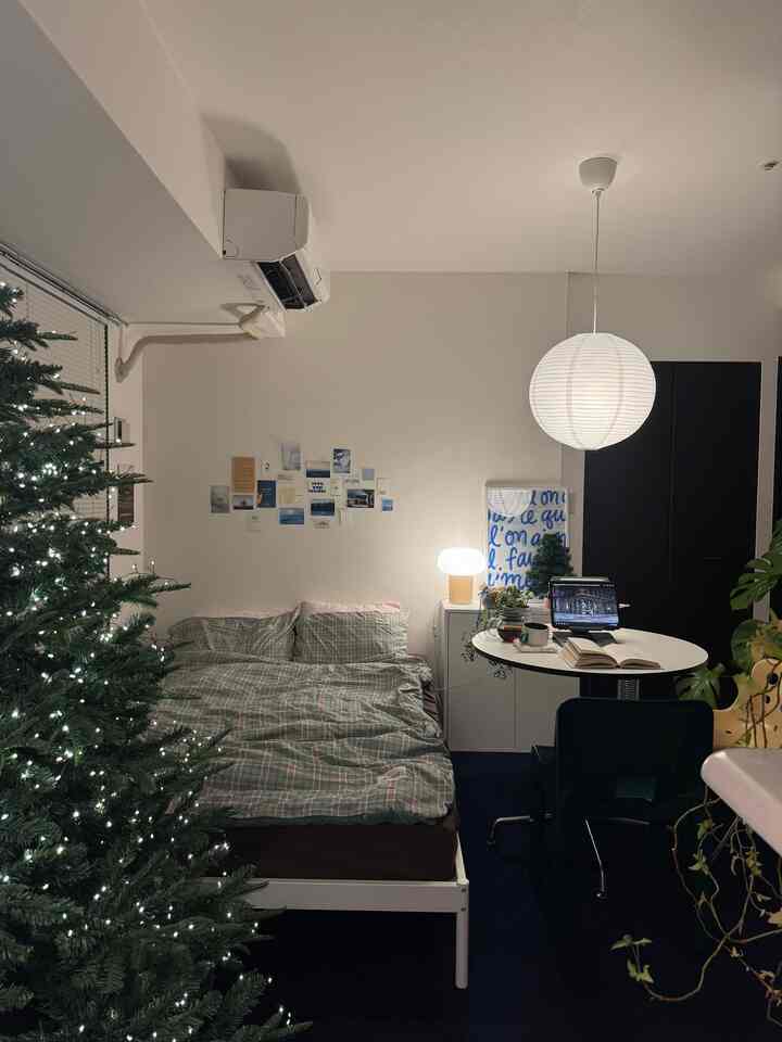 白とネイビーカラーのワンルーム寝室、クリスマスツリーとシンプルな家具が配置された雰囲気のあるインテリア