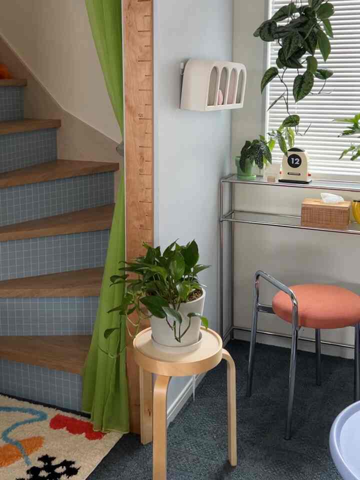 ナチュラルカラーと青い階段、緑の植物がある小さな階段横のスペースにオレンジのスツールが配置された雰囲気のあるインテリア