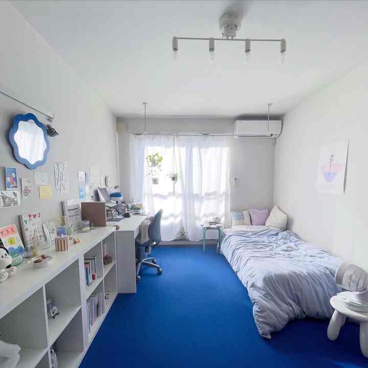 Bright white walls and ceiling with a blue carpet in an 8-tatami studio bedroom featuring a desk and bed in a tidy layout