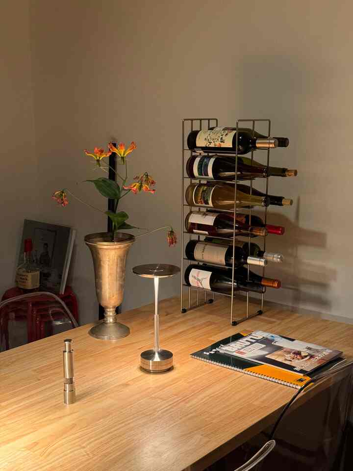 ナチュラルな木製ダイニングテーブルの1LDK一人暮らし空間、ゴールドの花瓶とワインラックが配置された