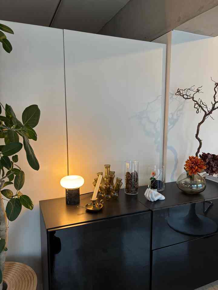 白い壁と黒い収納キャビネットのある空間、テーブルランプやさまざまな花瓶、植物が調和したナチュラルモダンなインテリア