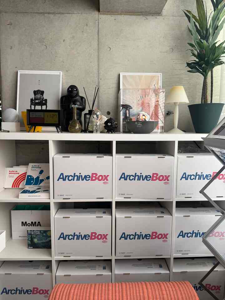 White and gray toned entrance featuring white archive boxes and bookshelf topped with objets and a table lamp in a mid-century modern style