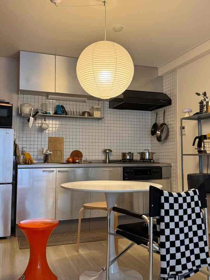 A white and light brown toned kitchen featuring a round dining table and orange stool in a mid-century modern style setting