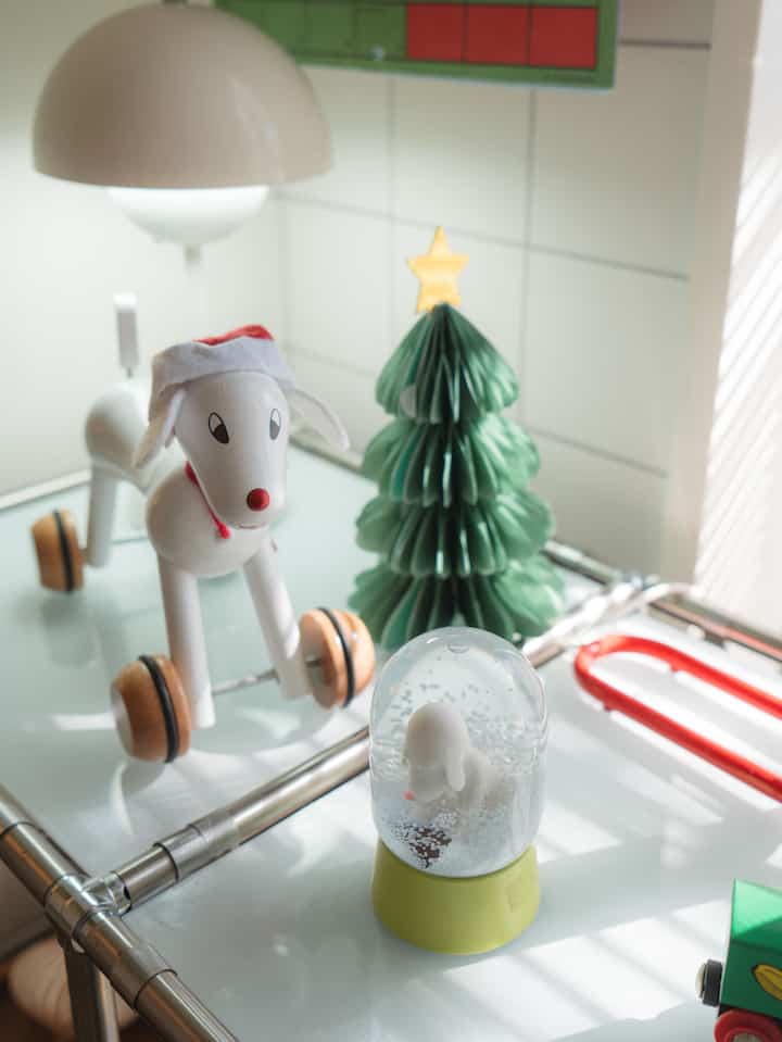 白い背景とクリスマス飾りが調和した空間に、犬の形の乗り物おもちゃと紙のクリスマスツリーが配置された雰囲気のあるインテリア