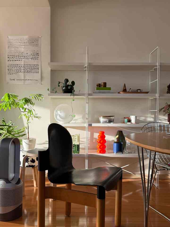 Warm wood tone mid-century modern dining room featuring a black chair, white shelving unit, and vibrant orange decor