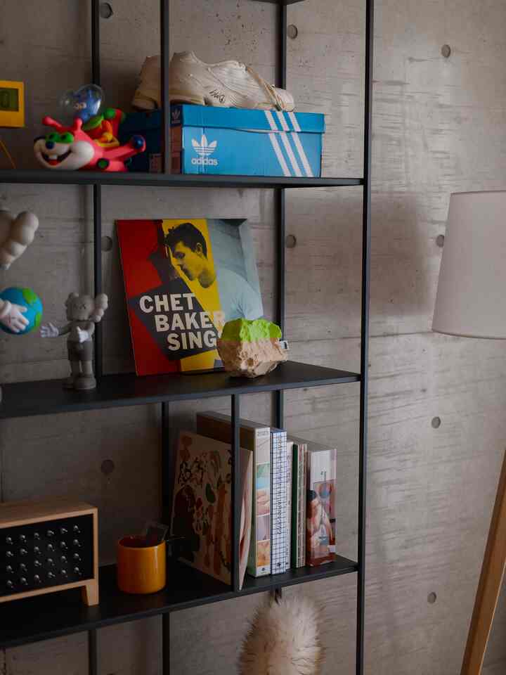 グレーのコンクリート壁と黒いメタル棚が配置された、一人暮らし向けのモダンなリビングスペース