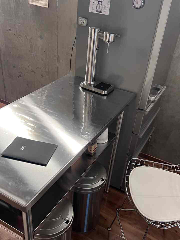 グレーとステンレスのトーンのキッチン空間、ステンレス作業台と自動ゴミ箱が配置された清潔感のあるモダンなインテリア